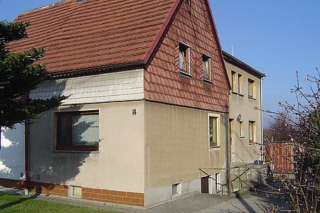 Doppelhaushälfte mit beiger Fassade im Unterschoss und verblasster, roter Vertäfelung im ersten Stock