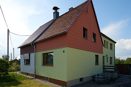 Doppelhaushälfte mit hellgrüner Fassade im Erdgeschoss und roter Vertäfelung im ersten Stock