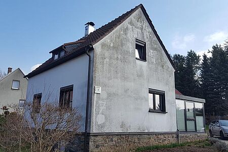 Hellblaues Einfamilienhaus mit stark verschmutzter Fassade und Wintergarten