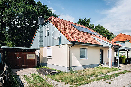 Einfamilienhaus mit frischer eierschalenfarbener Fassade im Erdgeschoss und türkiser Holzvertäfelung im oberen Stockwerk