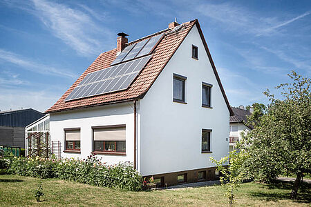 Weißes Einfamilienhaus mit Photovoltaikanlagen nach der Fassadensanierung