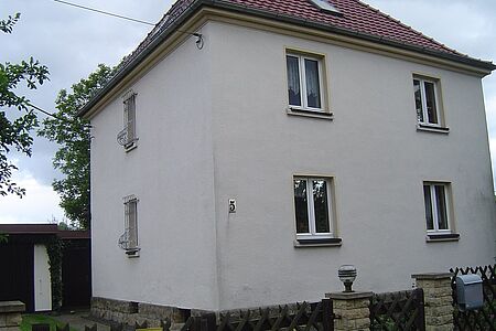 Mehrfamilienhaus mit Walmdach und weißer, verwitterter Fassade