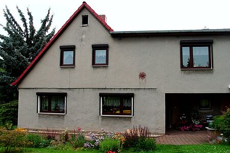 Einfamilienhaus mit Grünfläche im Vordergrund, graue Fassade mit einigen Rissen