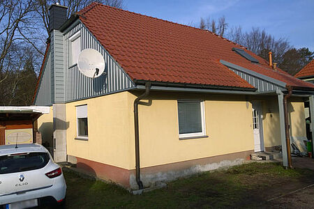 Einfamilienhaus mit leicht verschmutzter sonnengelber Fassade und graublauer Vertäfelung