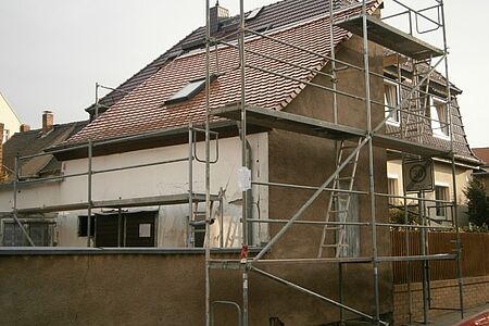 Braune Außenwand mit Mauer, an der ein Baugeländer steht.