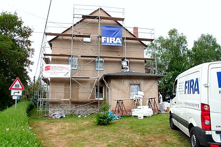 Großes ungestrichenes Mehrfamilienhaus während der Fassadensanierung mit Baugerüst