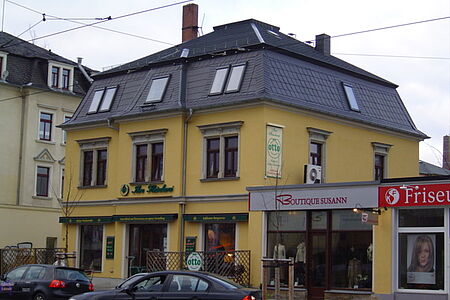 Wohn- und Geschäftshaus mit gelbem Anstrich und schwarzem Ziegeldach