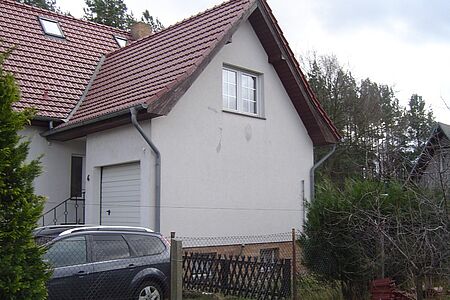 Verwinkeltes Wohnhaus mit alter, weißer Fassade im Grünen