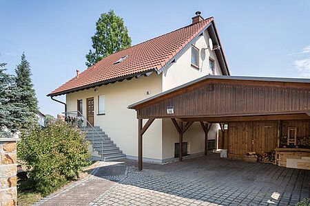 Pastellgelbes Wohnhaus mit geradem Treppenaufgang und angebautem Holzcarport