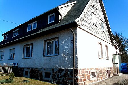 Rustikale weiße Fassade mit zahlreichen dunklen Stellen aufgrund von Witterungsschäden