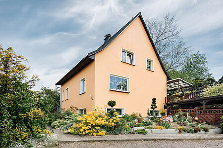 Apricotfarbenes Wohnhaus mit spitzem Satteldach und gepflegtem Garten