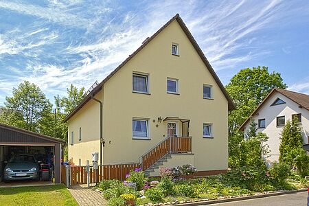 Hellgelbes Einfamilienhaus mit drei Stockwerken, Garage und Garten