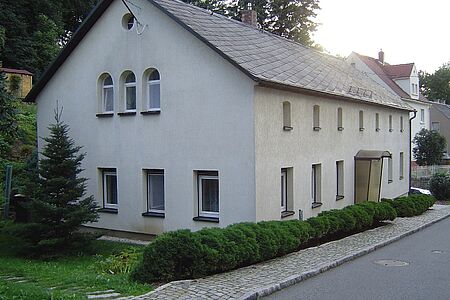 Mehrfamilienhaus mit veralteter Fassade in hellem Grau