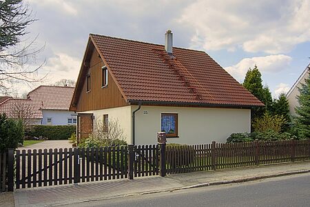 Einfamilienhaus mit Fassade in sehr hellem Pastellgelb im Erdgeschoss und hellbrauner Holzertäfelung im Obergeschoss