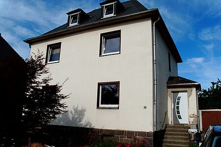 Frontansicht eines weißen Hauses mit kleinem Hauseingang-Anbau