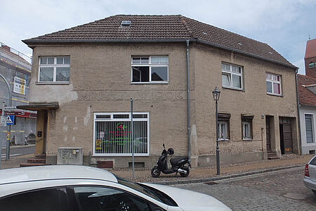 Braun verputztes Haus mit Gewerbeflächen im Erdgeschoss und bröckelnder Fassade