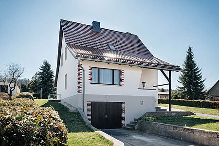 Einfamilienhaus mit hellgrauer Garage im Untergeschoss und frischer, weißer Fassade