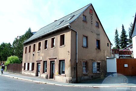 Heruntergekommenes Mehrfamilienhaus mit beschädigter Fassade und blätternden Fensterläden