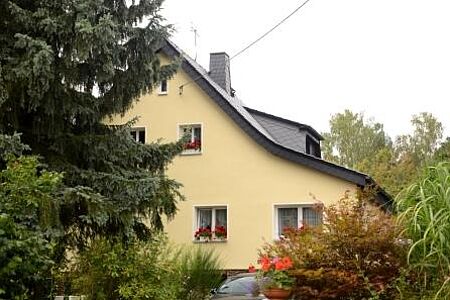 Blassgelbes Haus mit mehreren Fenstern und roten Blumen davor