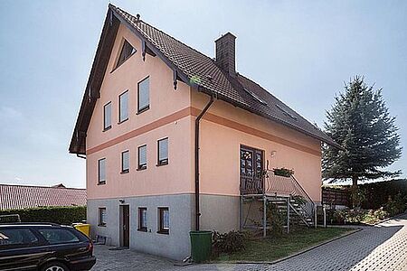 Vierstöckiges Wohnhaus mit grauer Fassade im unteren und pastell-korallefarbener Fassade in den oberen Stockwerken