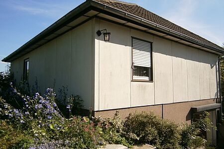 Eckansicht eines kleinen Einfamilienhauses mit dunklen Flecken an Fassade