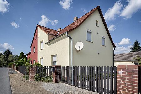 Doppelhaus mit roter Fassade auf der einen und pastellgelber Fassade auf der anderen Hälfte