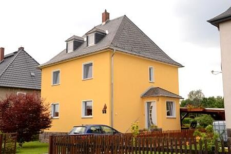 Kompaktes Einfamilienhaus mit gelber Fassade und blauem Auto davor
