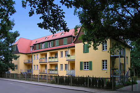 Saniertes Mehrfamilienhaus mit gelber Fassade, rotem Dach und grünen Fensterläden