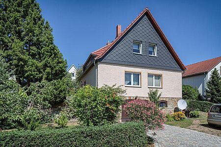 Wohnhaus mit dunkelgrau vertäfeltem ersten Stock, beiger Fassade im Erdgeschoss und Klinkern im Untergeschoss