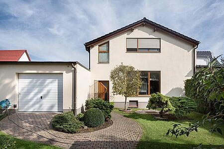 Eierschalenfarbenes Wohnhaus mit flachem Sattendach und Garage