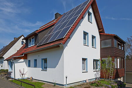 Weißes Wohnhaus mit drei Stockwerken und Photovoltaik-Anlage