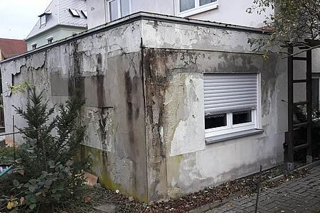 Abschnitt eines Hauses mit stark verwitterter, bröckelnder und fleckiger Fassade