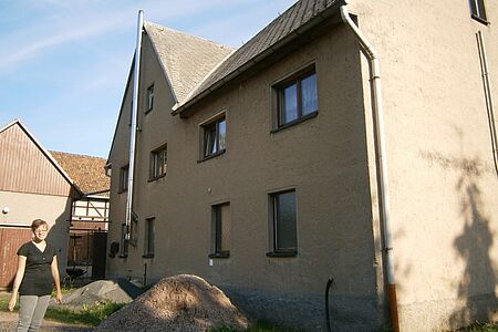 Frau steht an der Seite eines Einfamilienhauses mit brauner Fassade