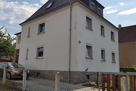 Weißes Mehrfamilienhaus mit sanierungsbedürftiger, leicht bröckelnder Fassade