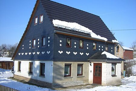 Verschneites Einfamilienhaus mit mehreren dunklen Stellen an der Fassade