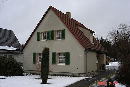 Ehemals weißes Wohnhaus mit stark verschmutzter Fassade und grünen Holzfensterläden