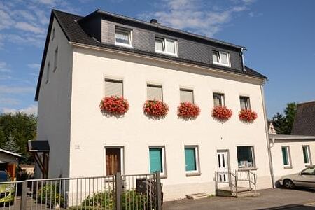 Weißer Hauswand mit roten Blumen vor den Fenstern im ersten Stock