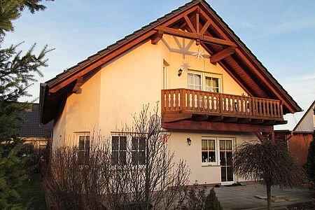 Wohnhaus mit Holzbalkon und Fassade in verschiedenen, hellen Orangetönen