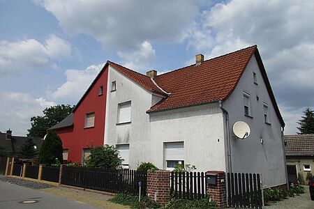 Doppelhaus mit roter Fassade auf der einen und schmutzig-weißer Fassade auf der anderen Hälfte