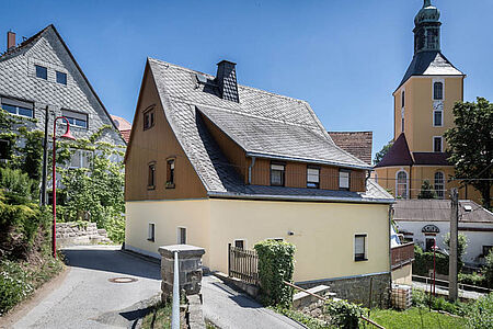 Wohnhaus in der Kleinstadt mit frischer, eierschalenfarbener Fassade im Erdgeschoss und Holzvertäfelung im ersten Stockwerk
