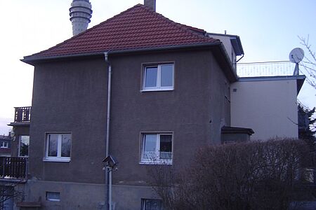 Mehrstöckiges Wohnhaus mit Walmdach und Fassade in schmutzigem Grau-Braun