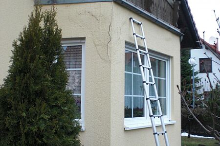 Leiter lehnt an Hauswand mit rissiger Fassade an der vorderen Ecke