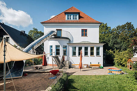 Kindergartengebäude mit ebenmäßiger Fassade in sehr hellem Pastellblau
