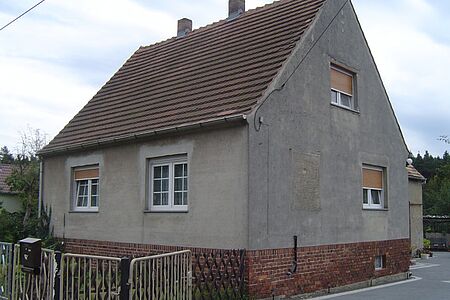 Graues Einfamilienhaus mit ungestrichener Fassade und spitzem Satteldach