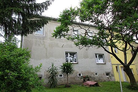 Grau verputztes Mehrfamilienhaus mit bröckelnder Fassade