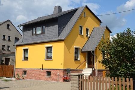 Einfamilienhaus mit frisch sanierter zinkgelber Fassade und kleinem Anbau für den Hauseingang an der Seite
