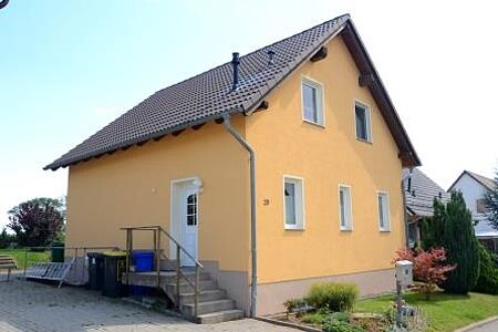 Einfamilienhaus mit gelber Fassade und kleiner Treppe zur Haustür