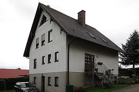 Vierstöckiges Wohnhaus mit beige-grauer Fassade im unteren und weißer, leicht verwitterter Fassade in den oberen Stockwerken 