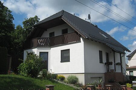 Weißes Wohnhaus mit drei Stockwerken, Erkerfenstern und Balkon
