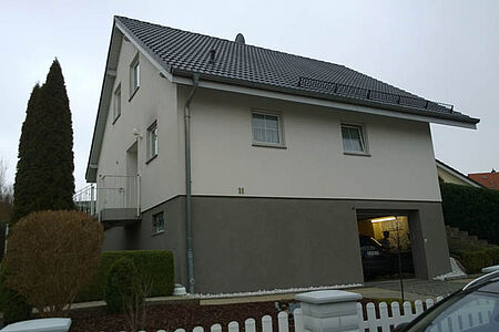 Dreistöckiges Einfamilienhaus mit schmutzig-weißer Fassade in den oberen Stockwerken und grauem Anstrich im Unterschoss